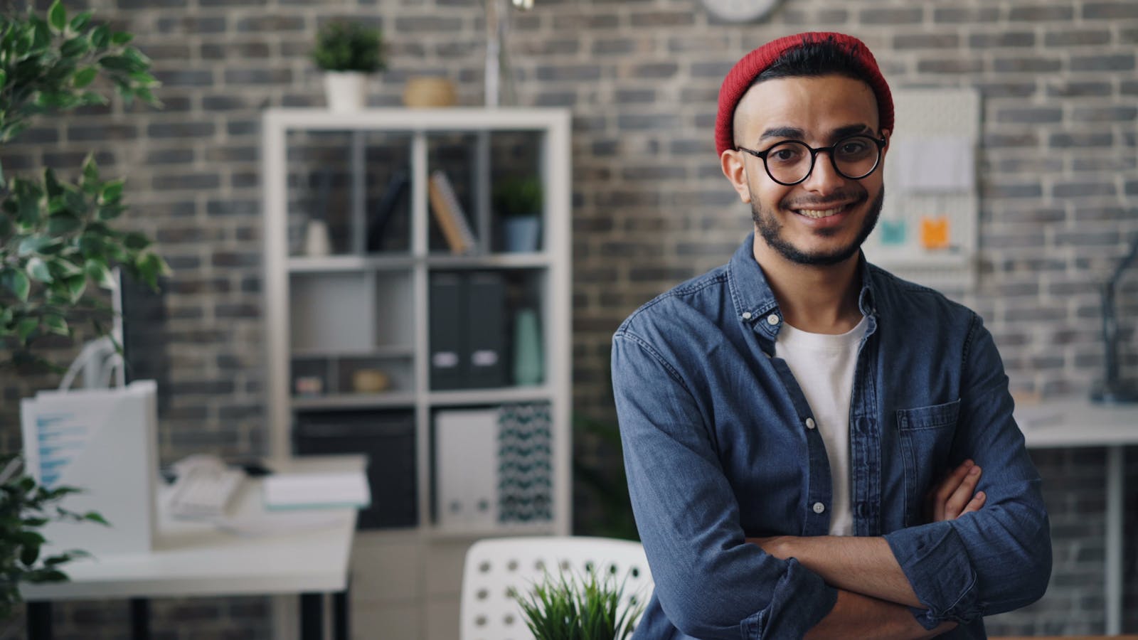 Confident young man in glasses smiling at camera in a stylish office setting.