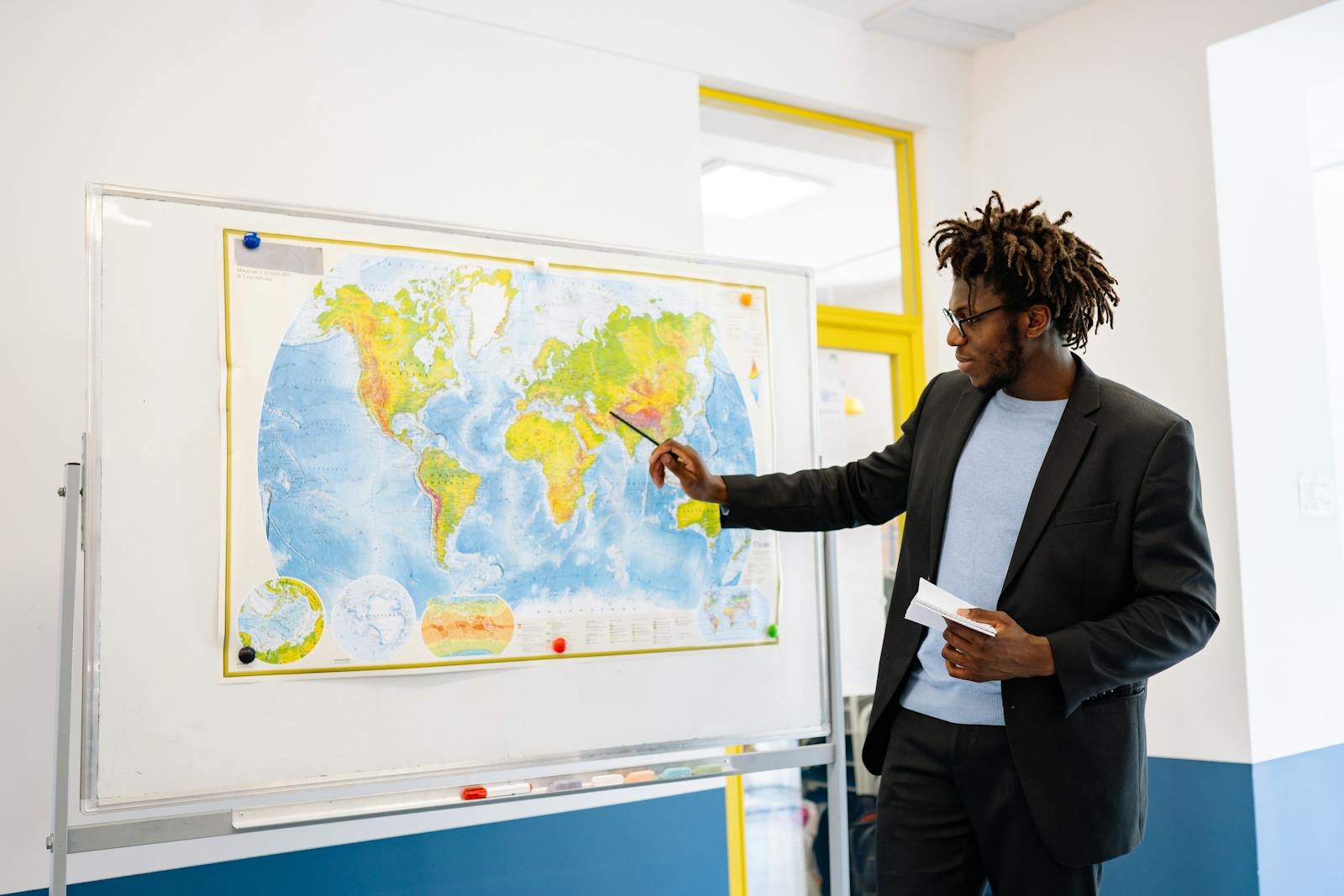 Teacher pointing at world map during classroom lesson, engaging students.